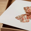 Vintage plaid bow in warm terracotta and cream tones against a white background, featuring intricate pattern detail with rustic charm perfect for farmhouse-inspired spaces.