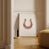 Elegant minimalist horseshoe in muted rose gold against white background, featuring detailed rivets and rustic finish, framed in natural wood for good luck charm in modern farmhouse decor.
