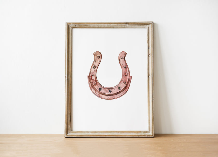 Elegant minimalist horseshoe in muted rose gold against white background, featuring detailed rivets and rustic finish, framed in natural wood for good luck charm in modern farmhouse decor.