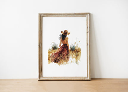 Solitary figure in flowing dress and wide-brimmed hat stands in desert landscape with burnt sienna, mustard and tan tones creating a serene, peaceful atmosphere against white background.