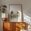 Serene watercolor scene of woman and horse in meadow, depicted in warm chestnut brown, sage green and gold tones on minimalist white background with rustic wooden frame elements