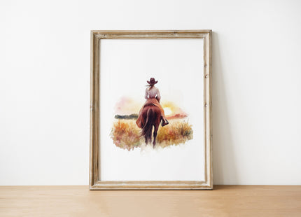 Watercolor silhouette of cowgirl riding horse at sunset with warm earth tones of sienna, pink and gold against white background, creating serene rustic ambiance perfect for farmhouse decor.