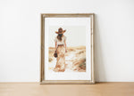 Serene vintage illustration of a solitary woman in wide-brimmed hat walking through desert landscape, rendered in soft sepia tones and sandy beige with minimalist sage green accents.
