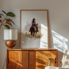 Watercolor cowgirl riding horse at sunset with soft pastel tones of blush pink, amber and lavender, creating a serene western-themed focal point against white space.