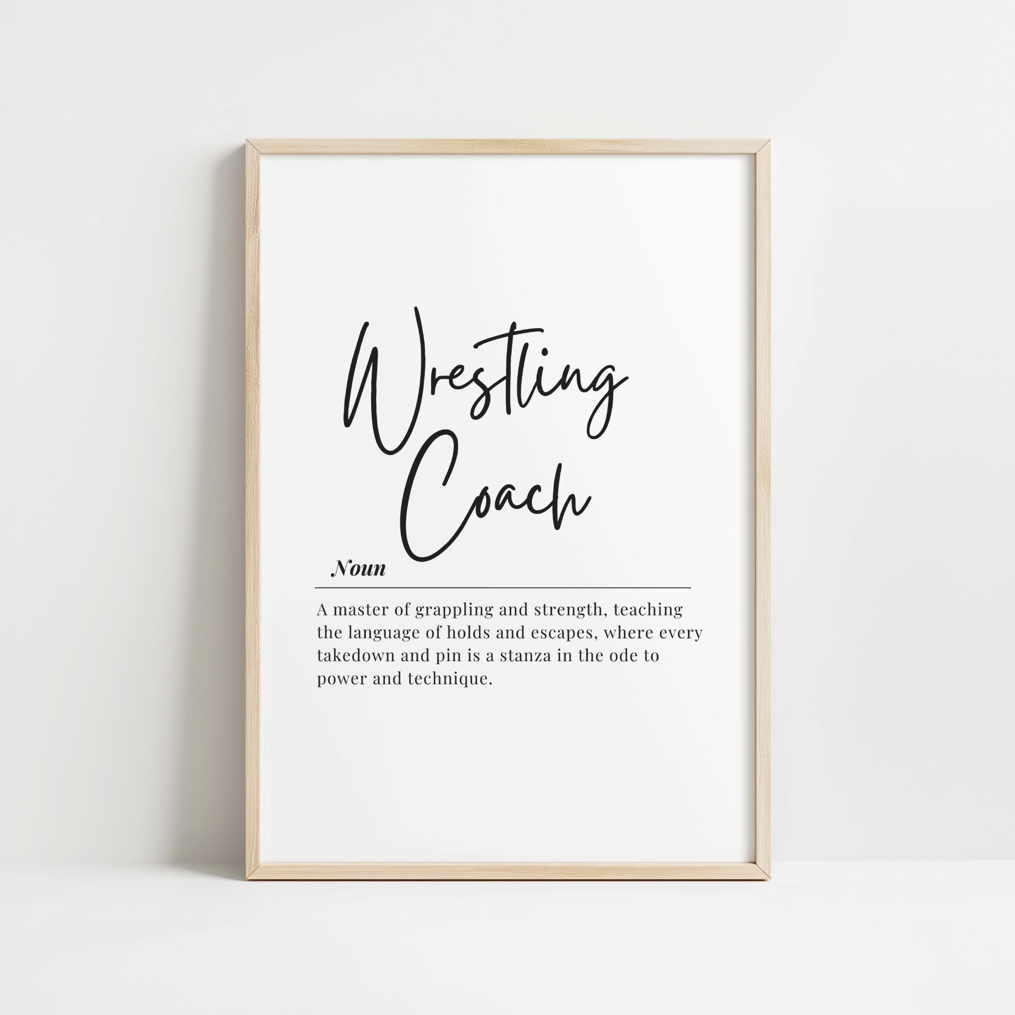 Minimalist black and white typography print with 'Wrestling Coach' in bold black script against a white background, paired with an inspirational serif font definition below, presented in a sleek wooden frame.